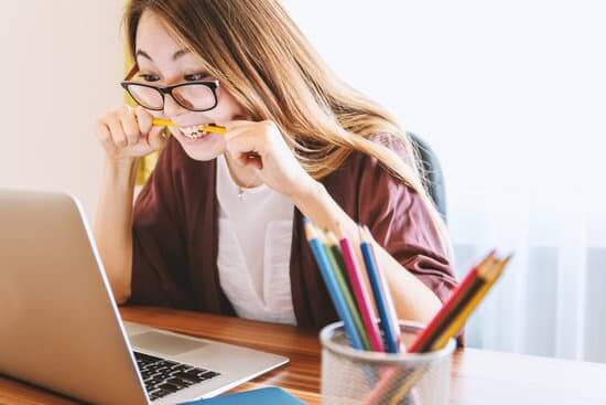 A woman staring at a laptop biting a pencil. 